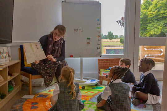 Pre-Prep Children learning in class with teacher holding up a book - Pre-Prep Classrooms - Space to Learn and Roam - News